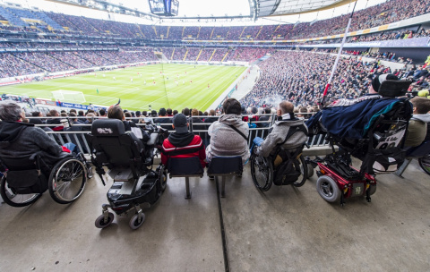 Fans im Rollstuhl blicken von ihren Plätzen auf das Spielfeld im Stadion von Eintracht Frankfurt.